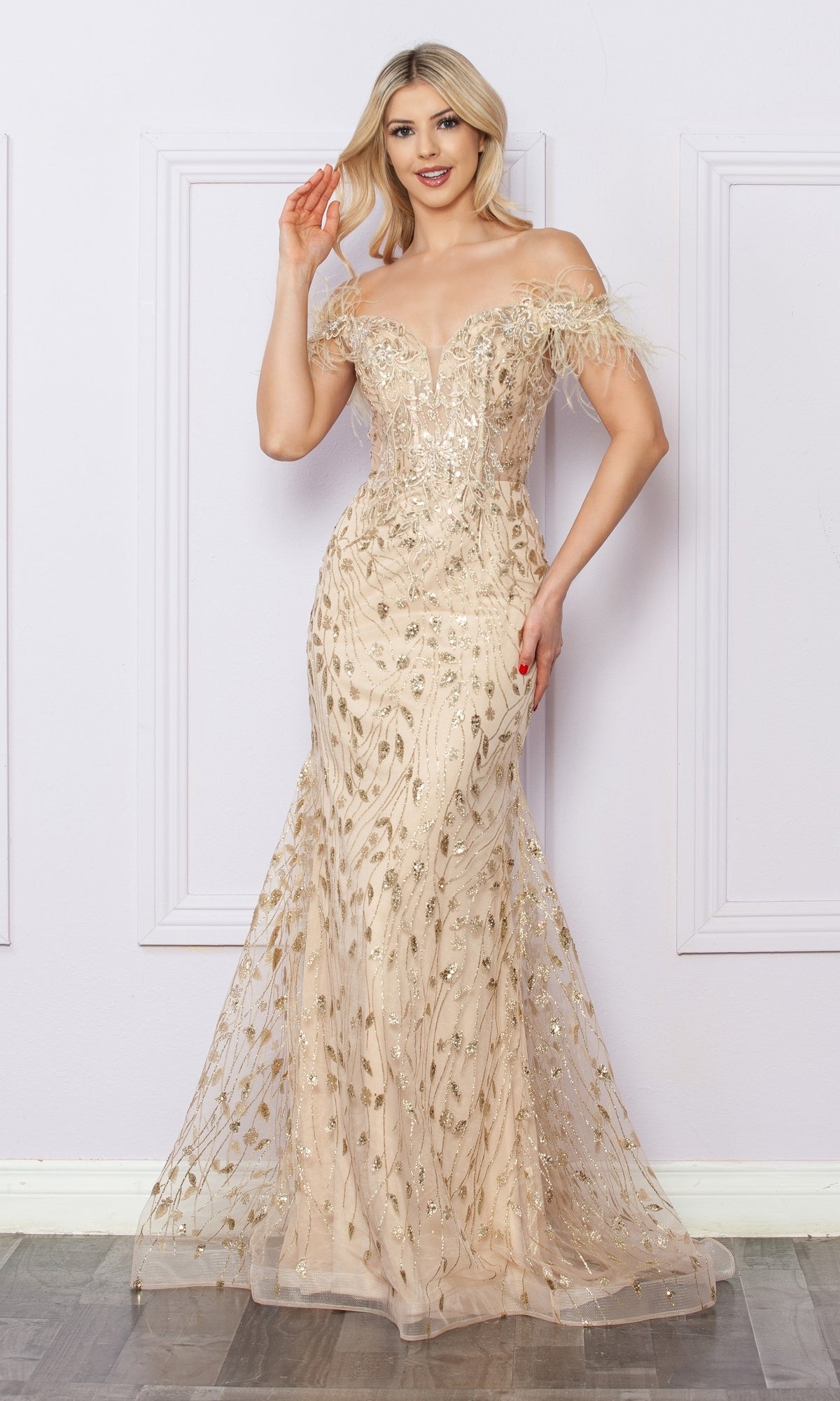 A woman poses indoors wearing the Sequined Glitter-Print Prom Dress: Nox Anabel L1255, featuring elegant off-the-shoulder styling, intricate gold detailing, and a sheer overlay.